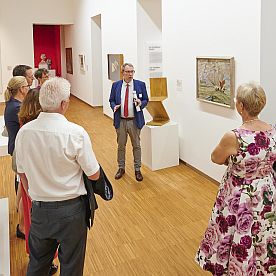 Eine kleine Gruppe von Förderen schauen sich mit einem Kurator das Gemälde von Lyonel Feininger an.