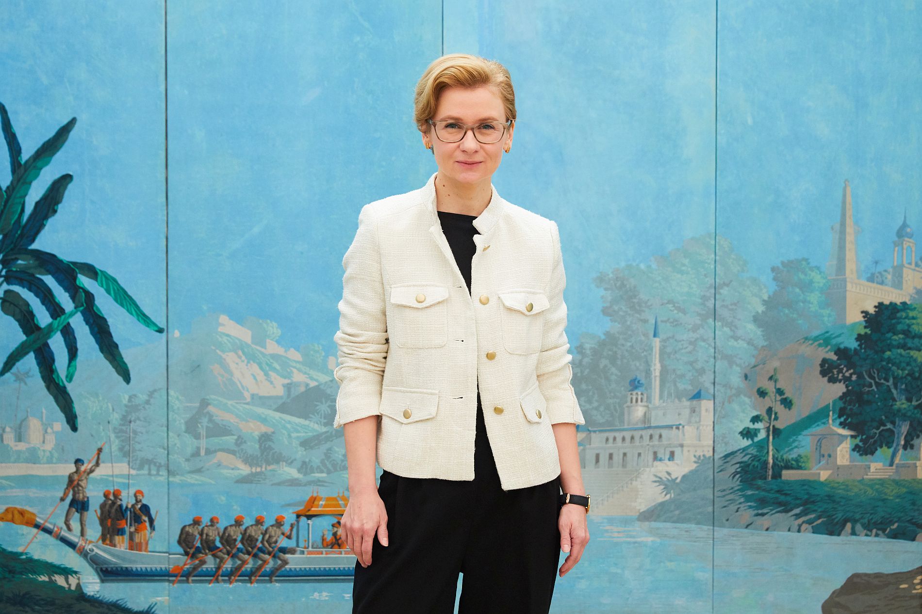 D. Karin Rhein steht vor einer orientalischen Bildtapete in der Dauerausstellung 19. Jahrhundert.