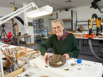 Ute Meyer-Buhr sitzt an einem Tisch in den archäologischen Restaurierungswerkstätten, auf dem Artefakte liegen.